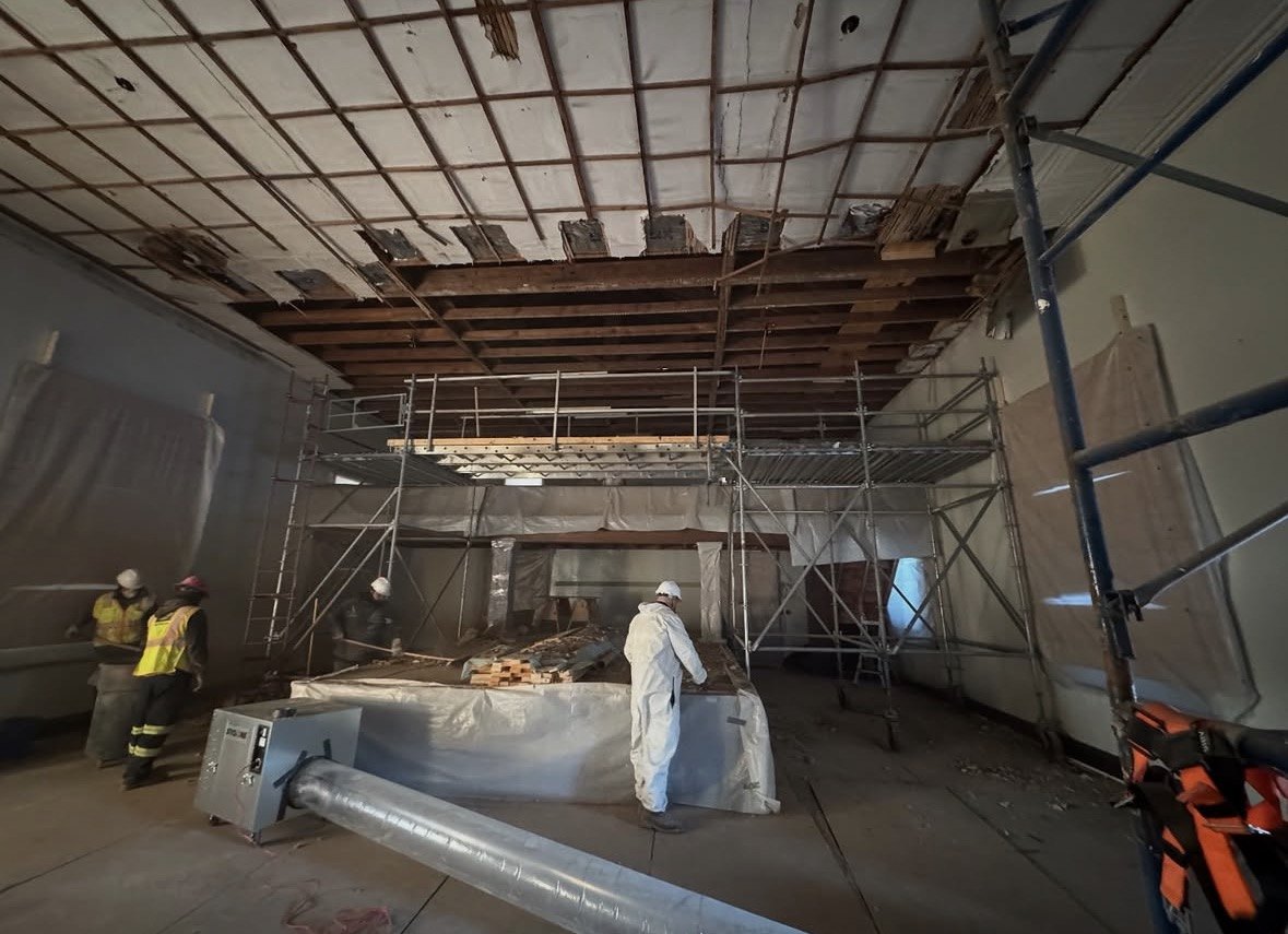 A-1 abatement crew in protective suits working inside a sealed containment with scaffolding and negative air machine