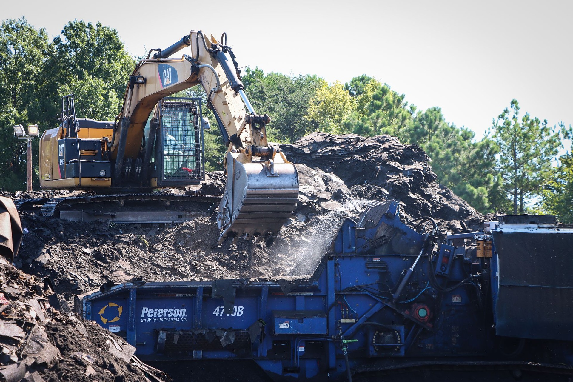 A-1 excavator feeding torn-off roofing shingles into a grinder