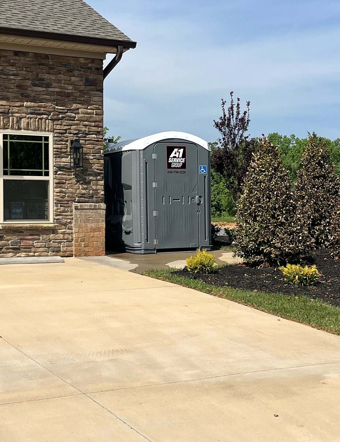 Gray A-1 ADA wheelchair-accessible portable toilet beside a stone house