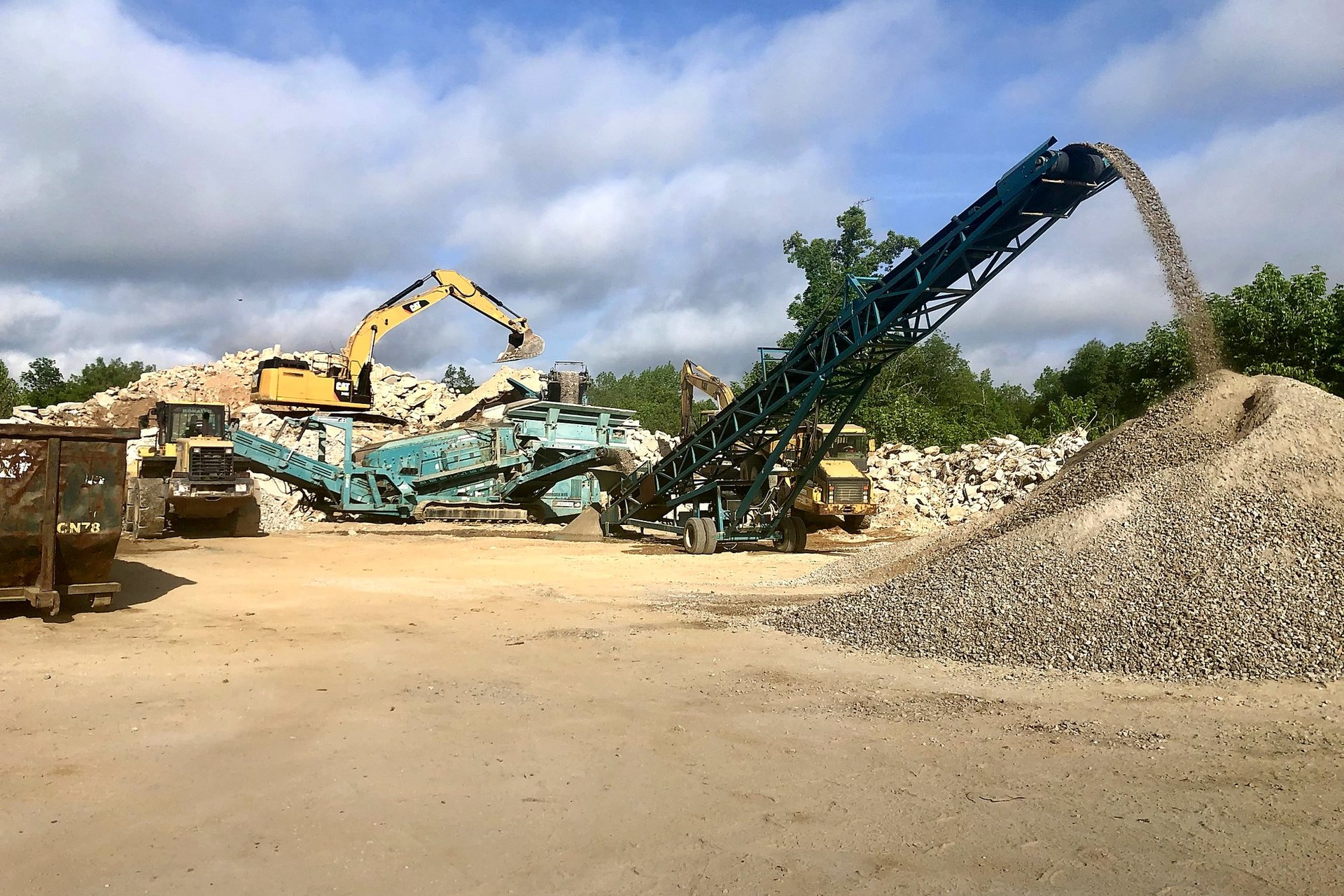 A-1 excavator feeding concrete into a crusher while a conveyor builds a pile of crushed stone
